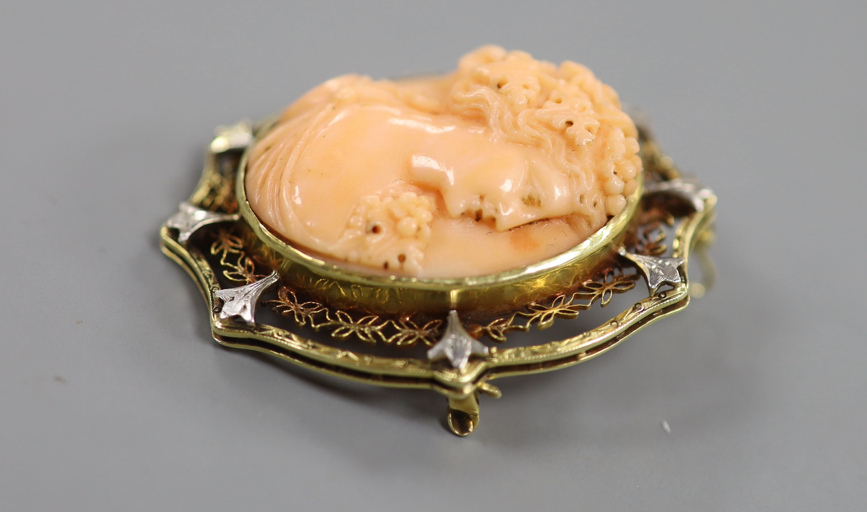 An early 20th century yellow and white metal mounted oval coral pendant brooch, carved with the bust of a lady to sinister